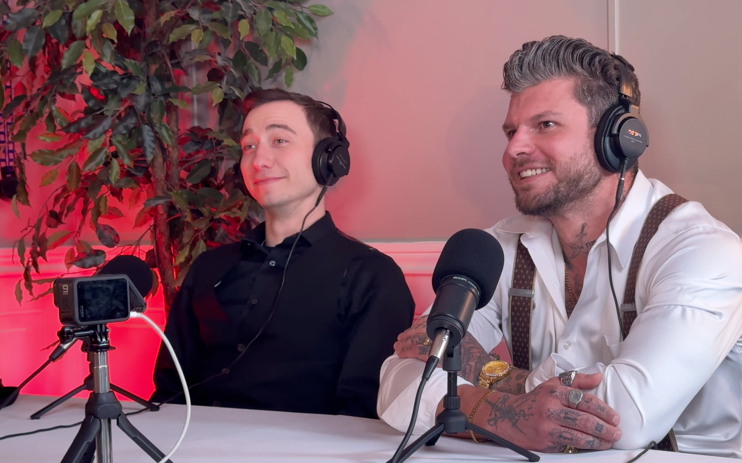 Isadore Goldsein and Alex Donnolo  wearing headphones, seated at a table with microphones, recording a podcast.