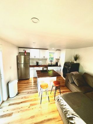 Open-concept kitchen and living area with white cabinets, wooden floor, stainless steel refrigerator, and brown sofa.