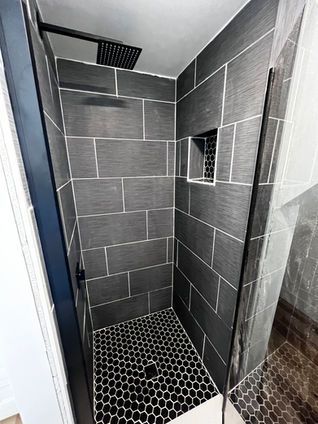 Dark gray tiled shower with black hexagon floor, showerhead, and niche.