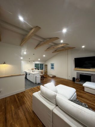 Spacious living room with wooden beams on the ceiling, white walls, and a fireplace.