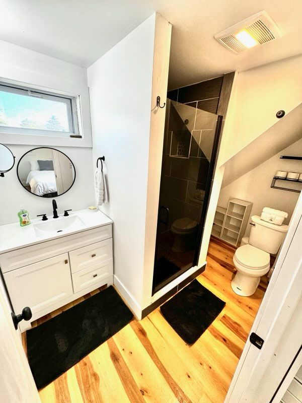 Bathroom with white vanity, black accents, glass shower, and wood flooring.