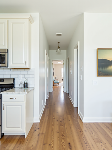 Hallway with hardwood floor, light gray walls, white cabinets, and artwork.