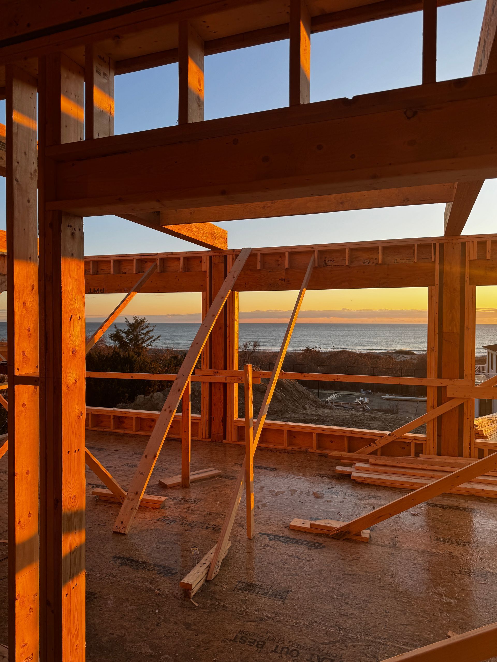 Wooden house frame under construction, with ocean view at sunset.