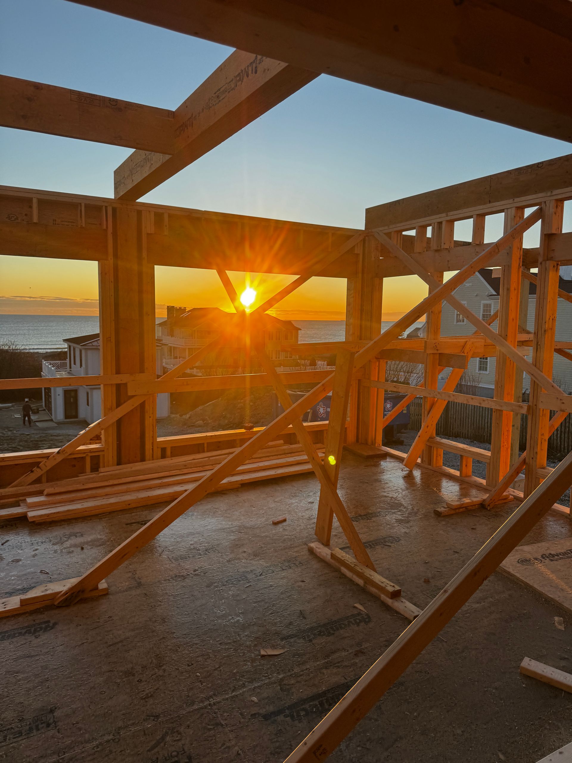 Construction site framing with sunset over ocean visible through window.