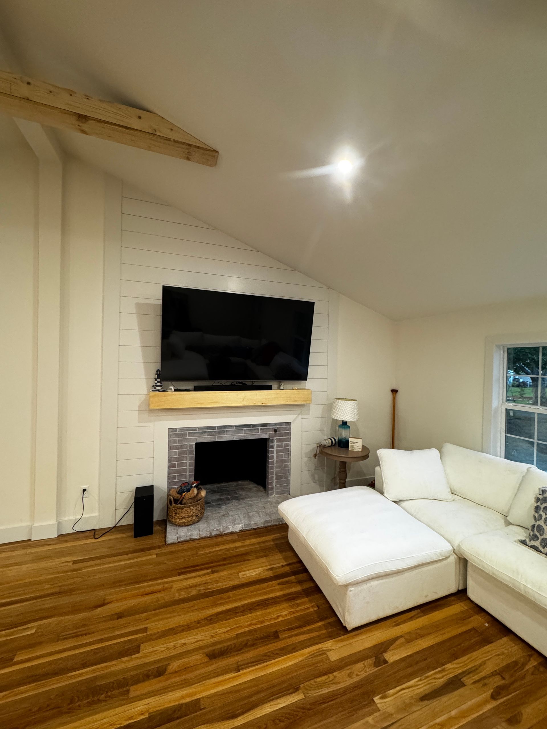 Living room with a fireplace, TV, and white sectional sofa. Hardwood floors and exposed beam.