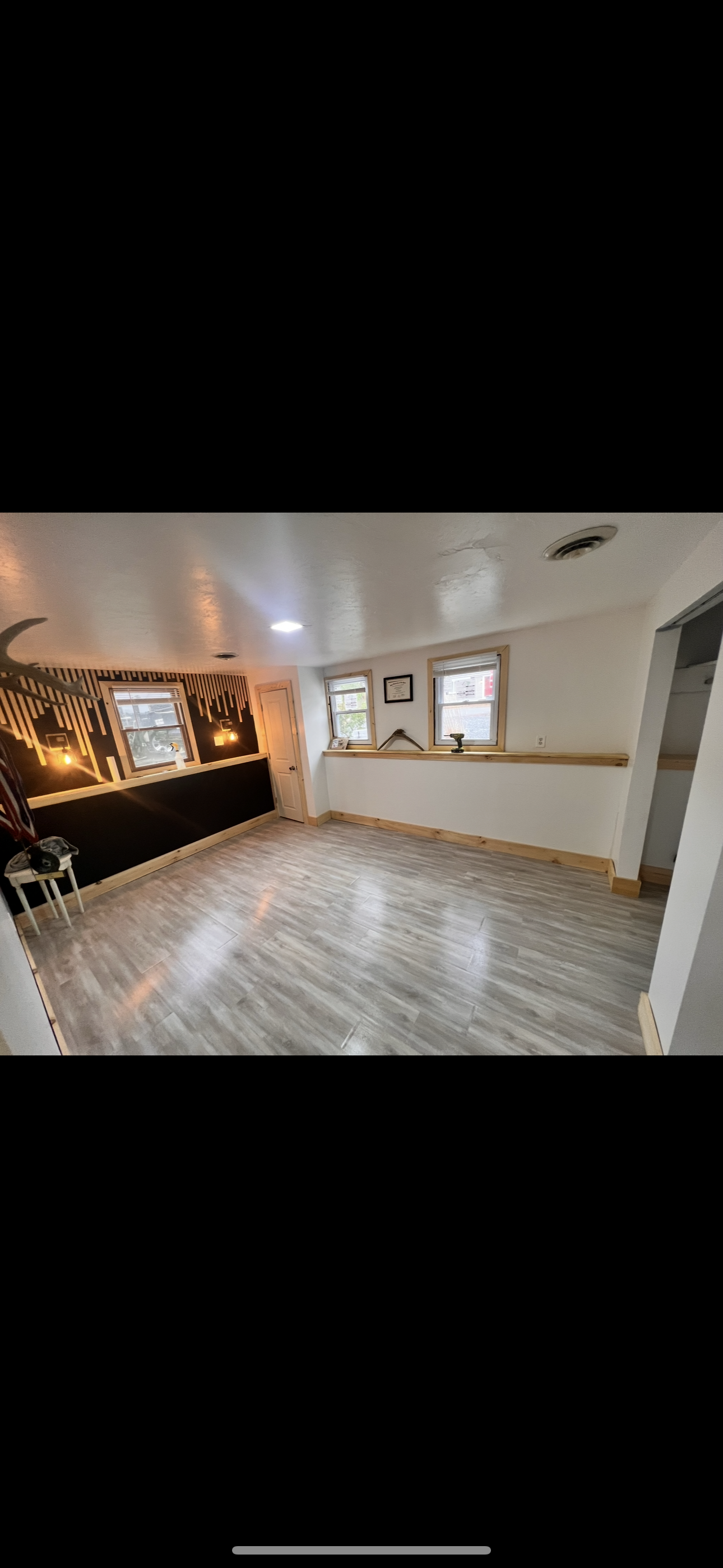 Empty room with gray flooring, two windows and a door. There is a dark colored countertop and wall on the left side of the room.