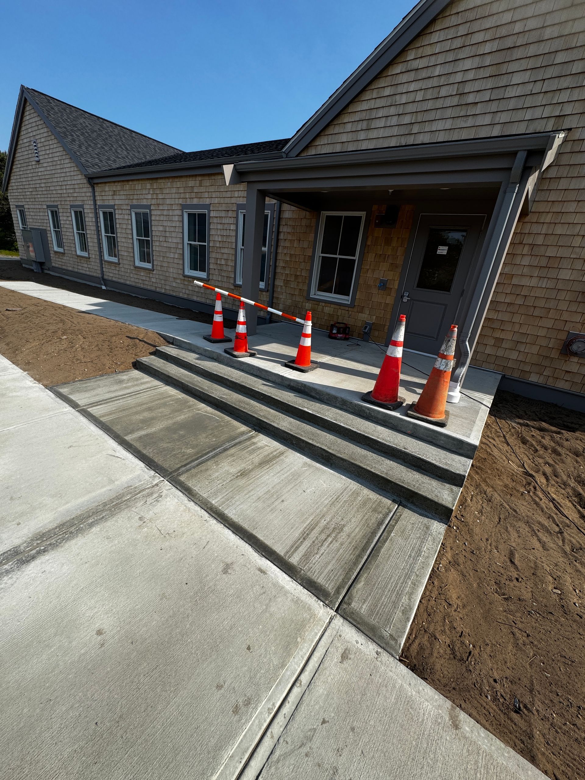 Exterior of building with brick facade. Concrete walkway blocked by orange traffic cones.