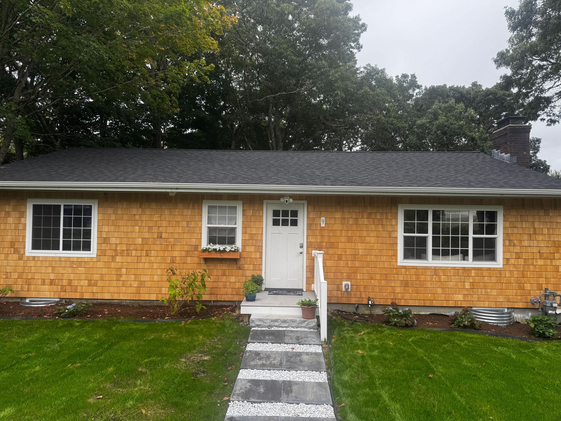 A one-story house with cedar siding, white trim, and a path leading to a white door.