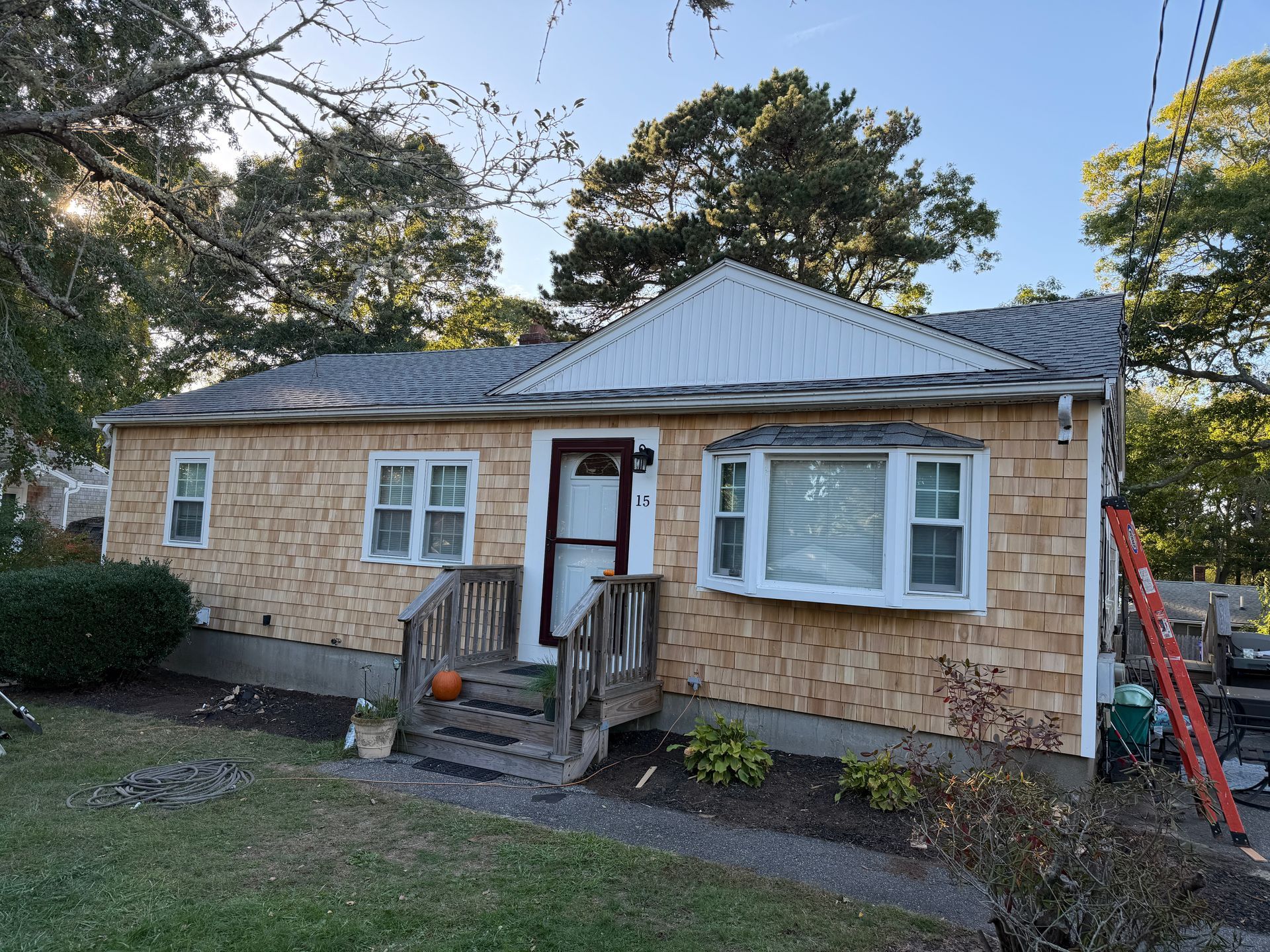 Tan shingled house with white trim. A bay window, porch, and orange ladder are visible.