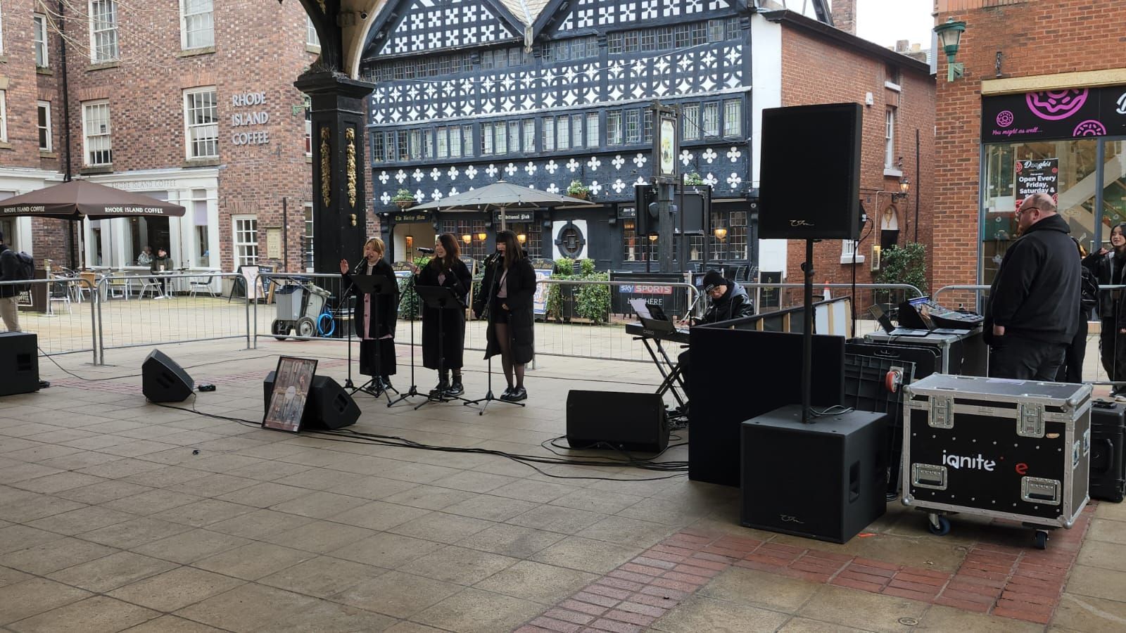 Band performing outdoors with a black and white Tudor-style building as a backdrop.