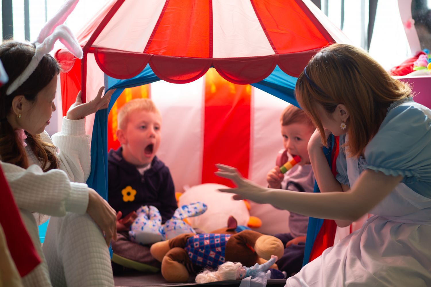 People in costumes interact with two children in a colorful play tent.