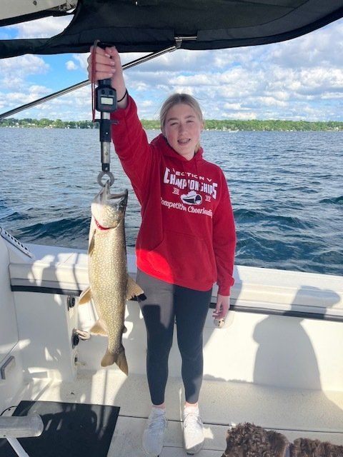 A girl in a red sweatshirt is holding a fish on a boat