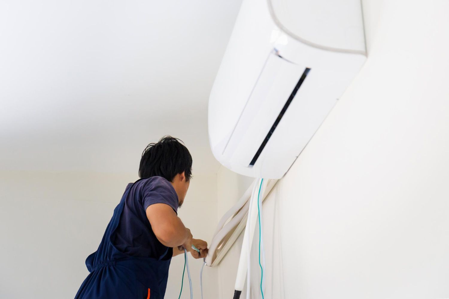 Person in blue overalls installing an air conditioning unit on a white wall.