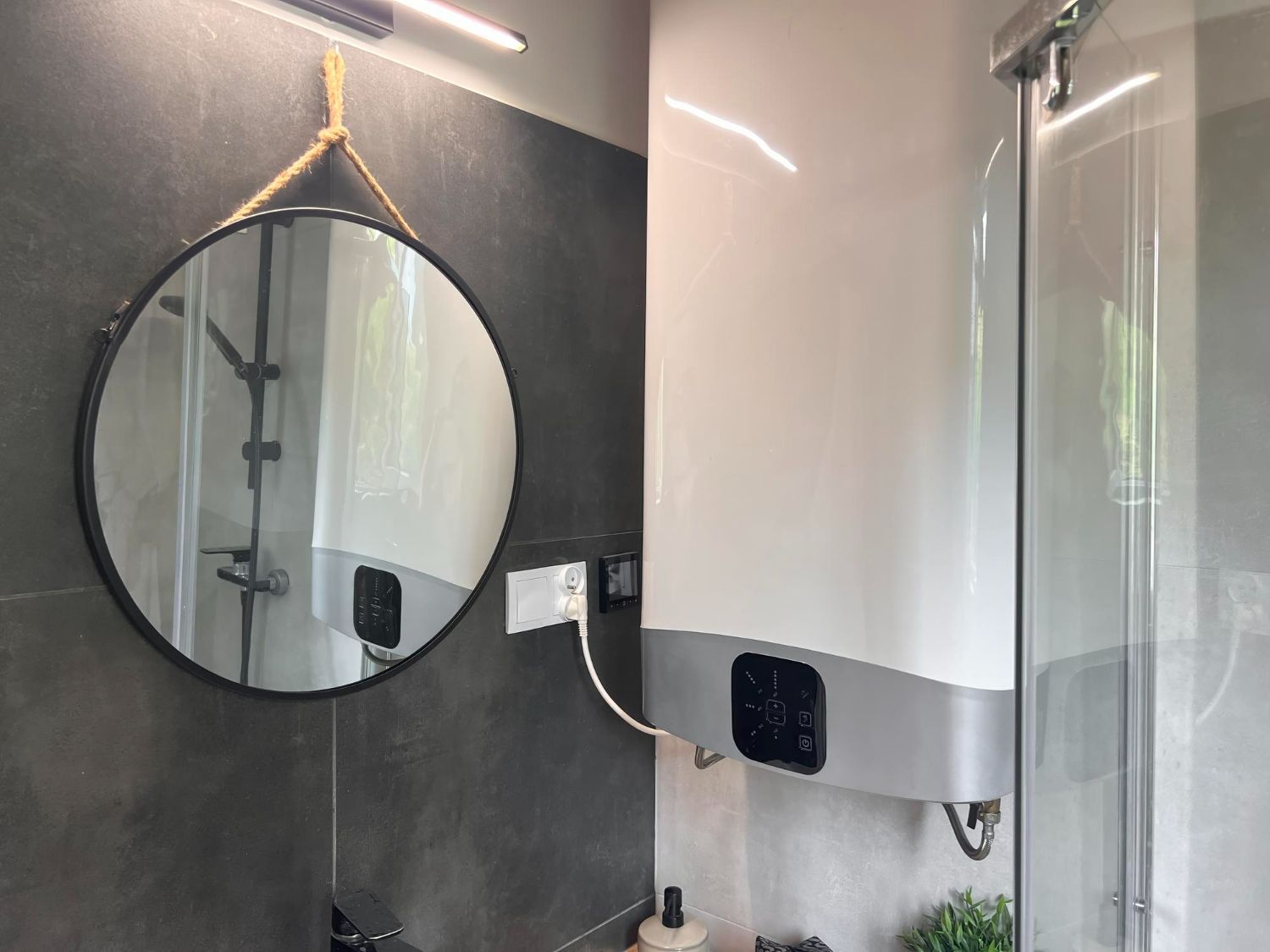 Bathroom with round mirror, water heater, and glass shower door.
