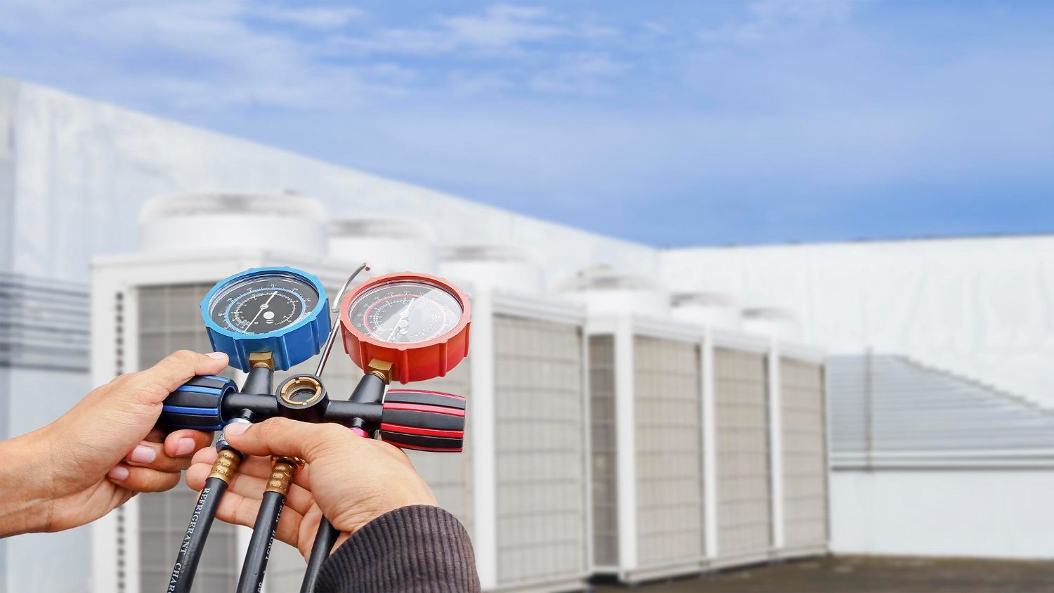 Technician using gauges to check an HVAC unit on a rooftop.