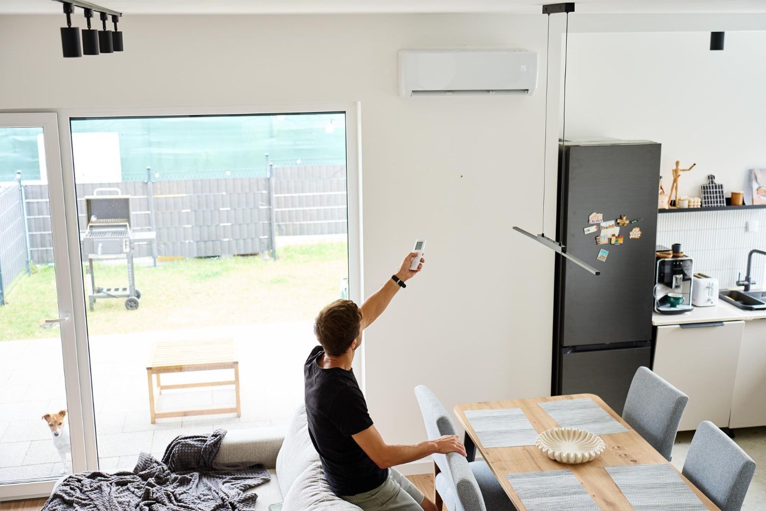 Man uses remote control to adjust AC unit in a modern dining room.