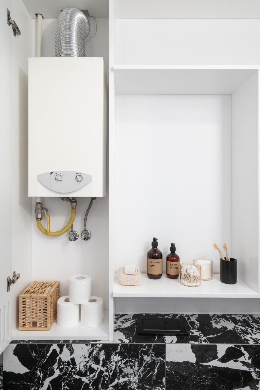 White cabinet with water heater and storage niche. Toiletries and toilet paper are on the shelf.