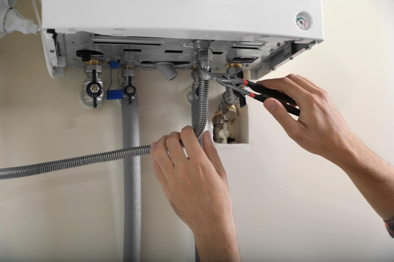 Person using pliers to work on pipes connected to a white wall-mounted boiler.