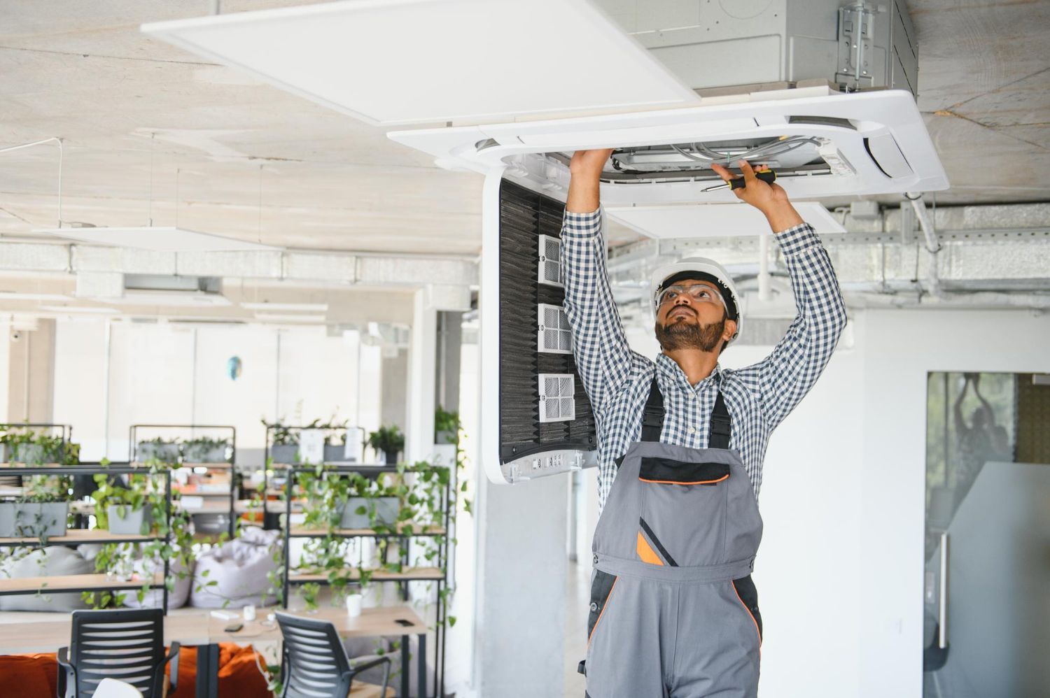 Man in work overalls installing ceiling air conditioning unit in an office.