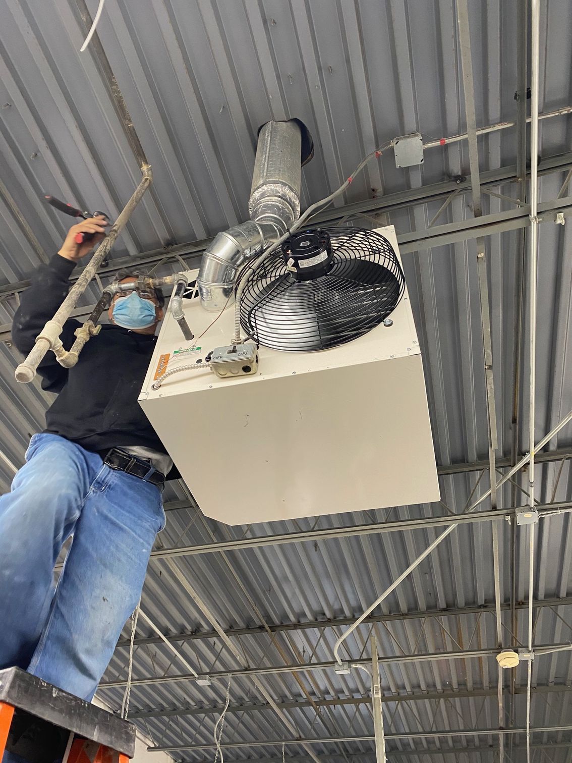 Person in hard hat and gloves working on pipes near a wall-mounted appliance.