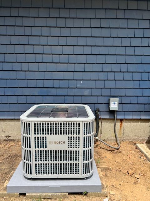 Man in work clothes pointing at a heat pump unit outside a building.