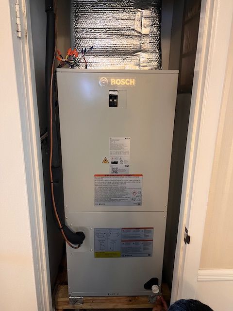 Woman warming hands by a wood-burning stove in a cozy, decorated room.
