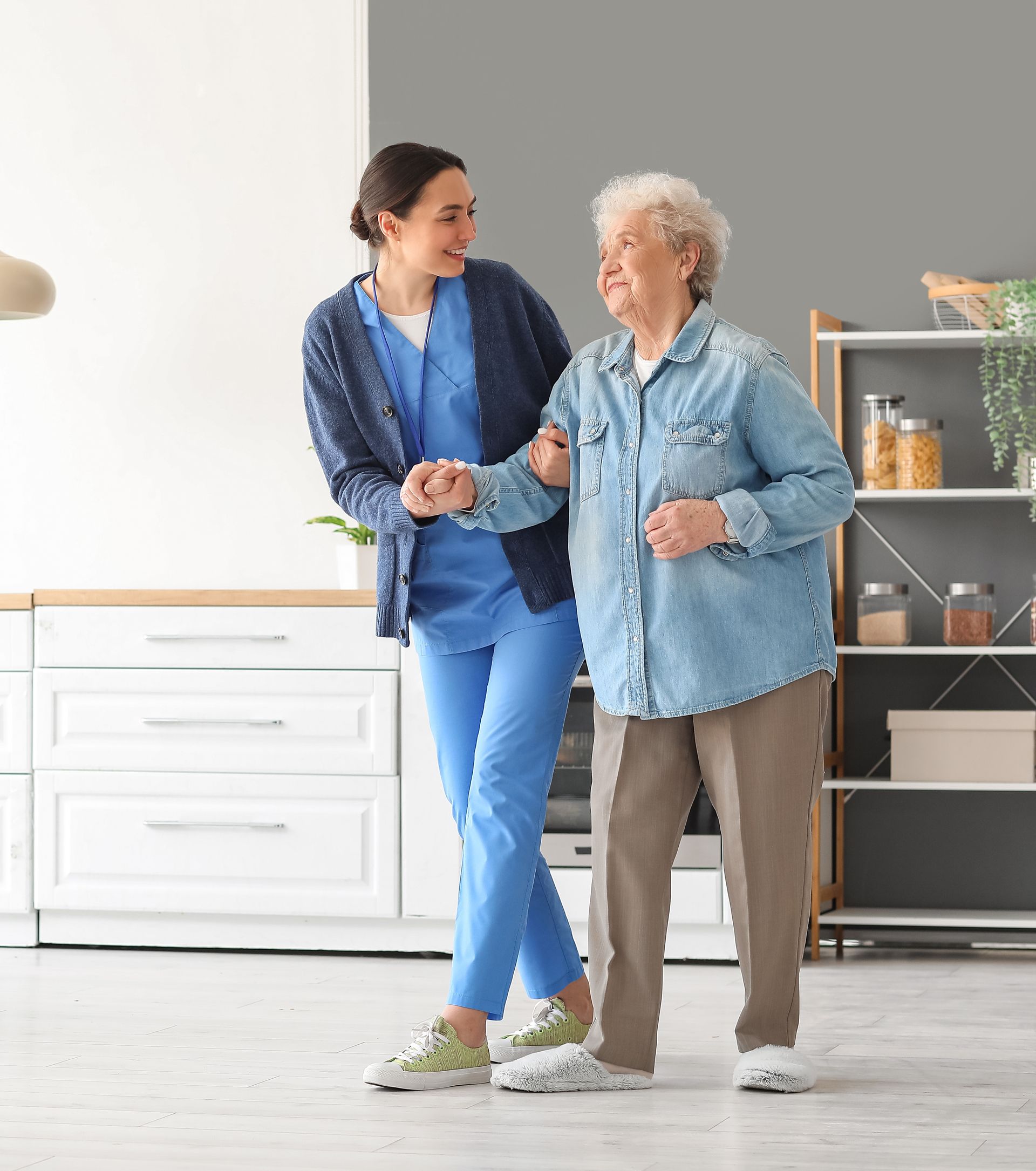 A nurse is helping an elderly woman walk in a kitchen.
