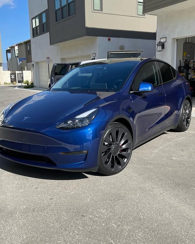 A blue tesla model y is parked in front of a building