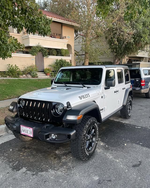 A white jeep wrangler is parked on the side of the road in front of a building.