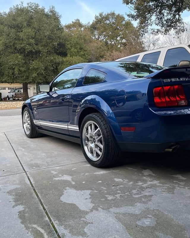 A blue mustang is parked in a driveway next to a white van.