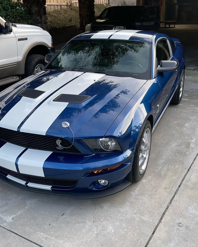 A blue mustang with white stripes is parked in a driveway