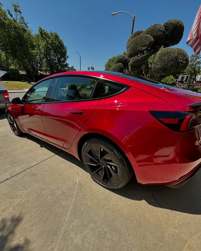 A red tesla model 3 is parked in a driveway.
