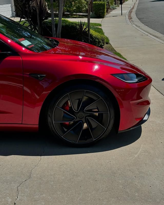 A red tesla model 3 is parked in a driveway