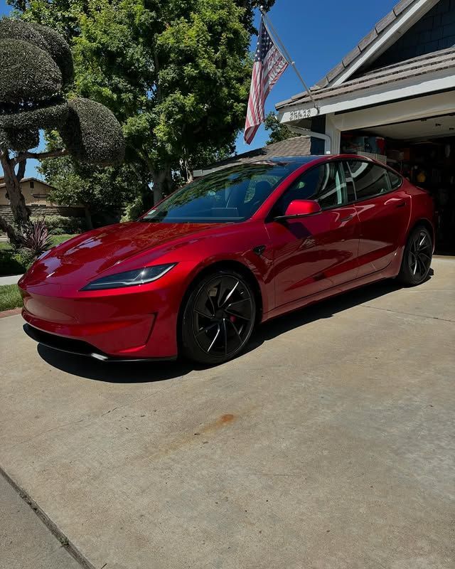 A red tesla model 3 is parked in front of a house