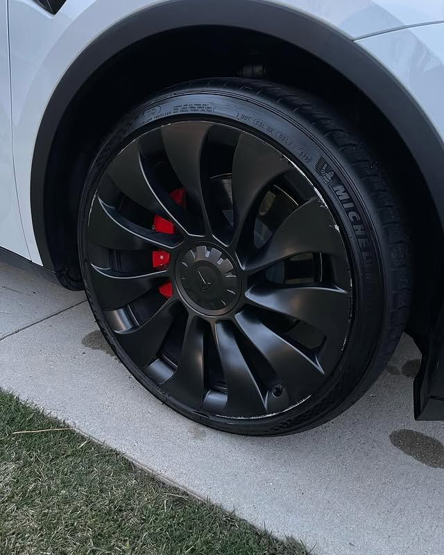 A white tesla model y with black wheels and red brake calipers