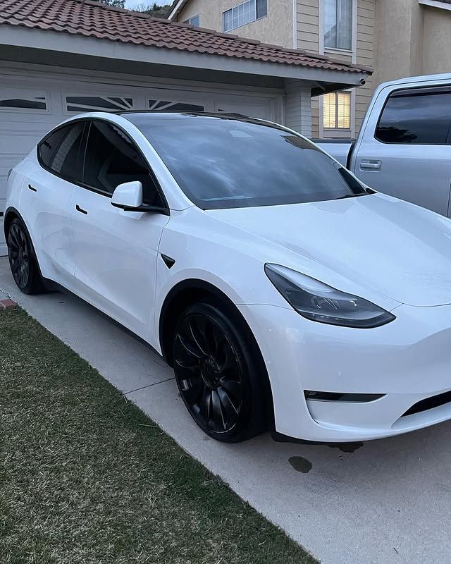 A white tesla model 3 is parked in front of a house.