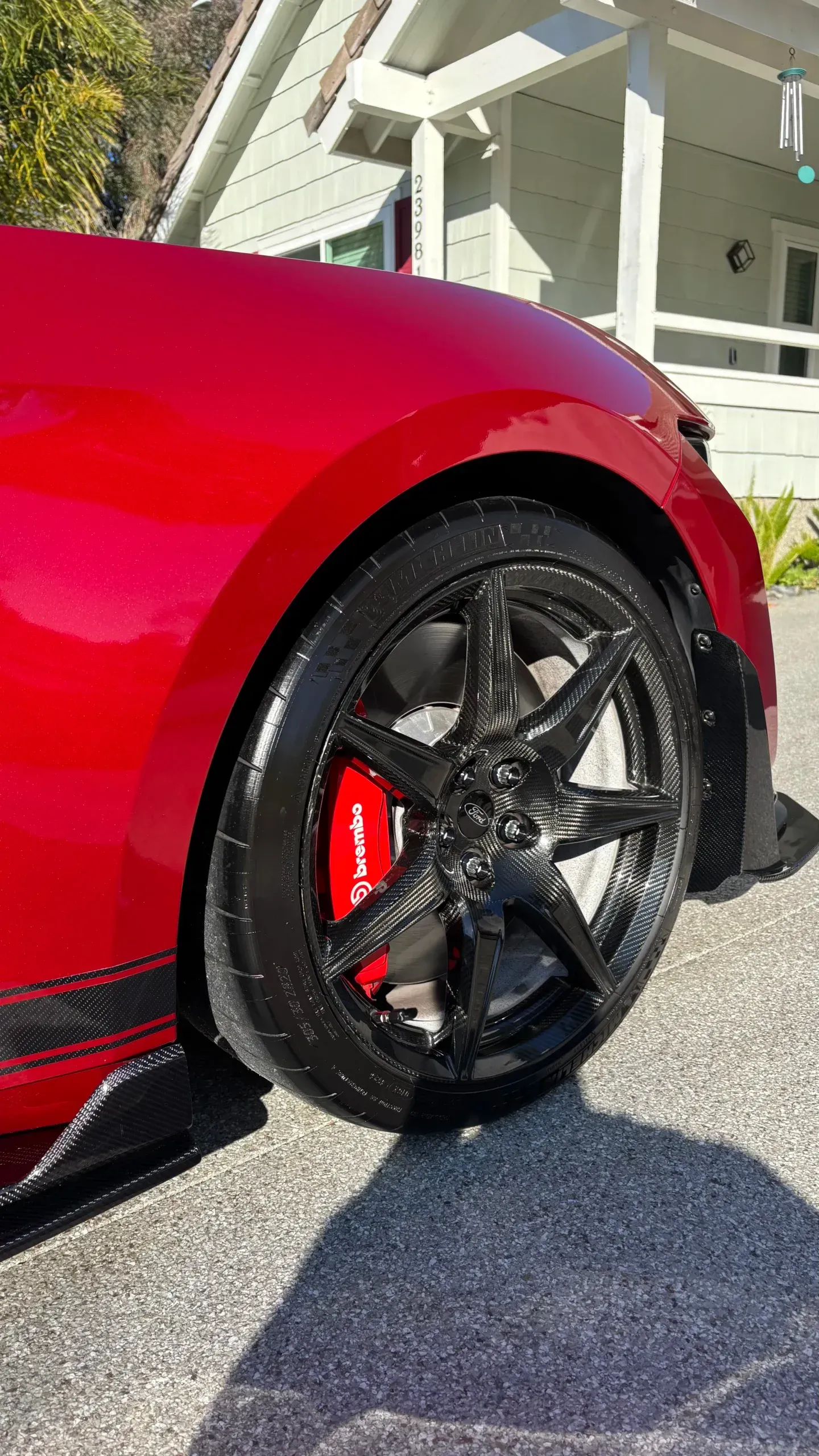 A red sports car with black wheels and red brake calipers is parked in front of a house.