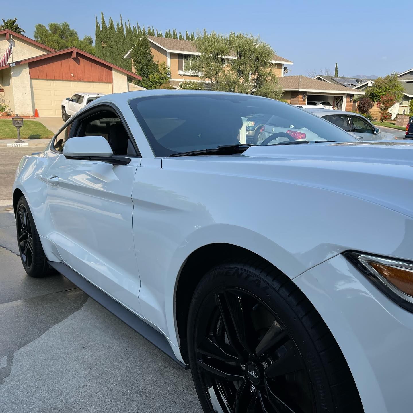 A white mustang is parked in a driveway in front of a house