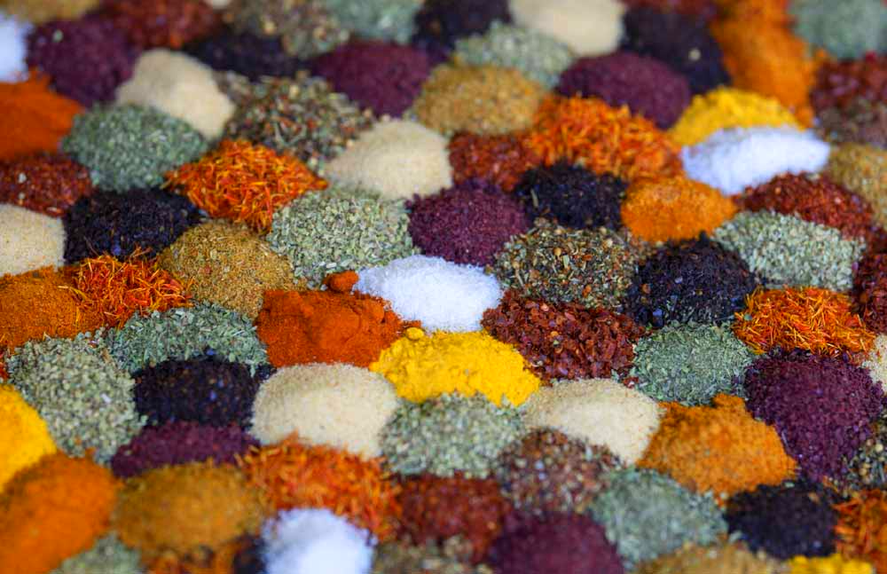 Aerial view of mounds of spices in different colours laid out next to each other so that it looks like a patchwork quilt