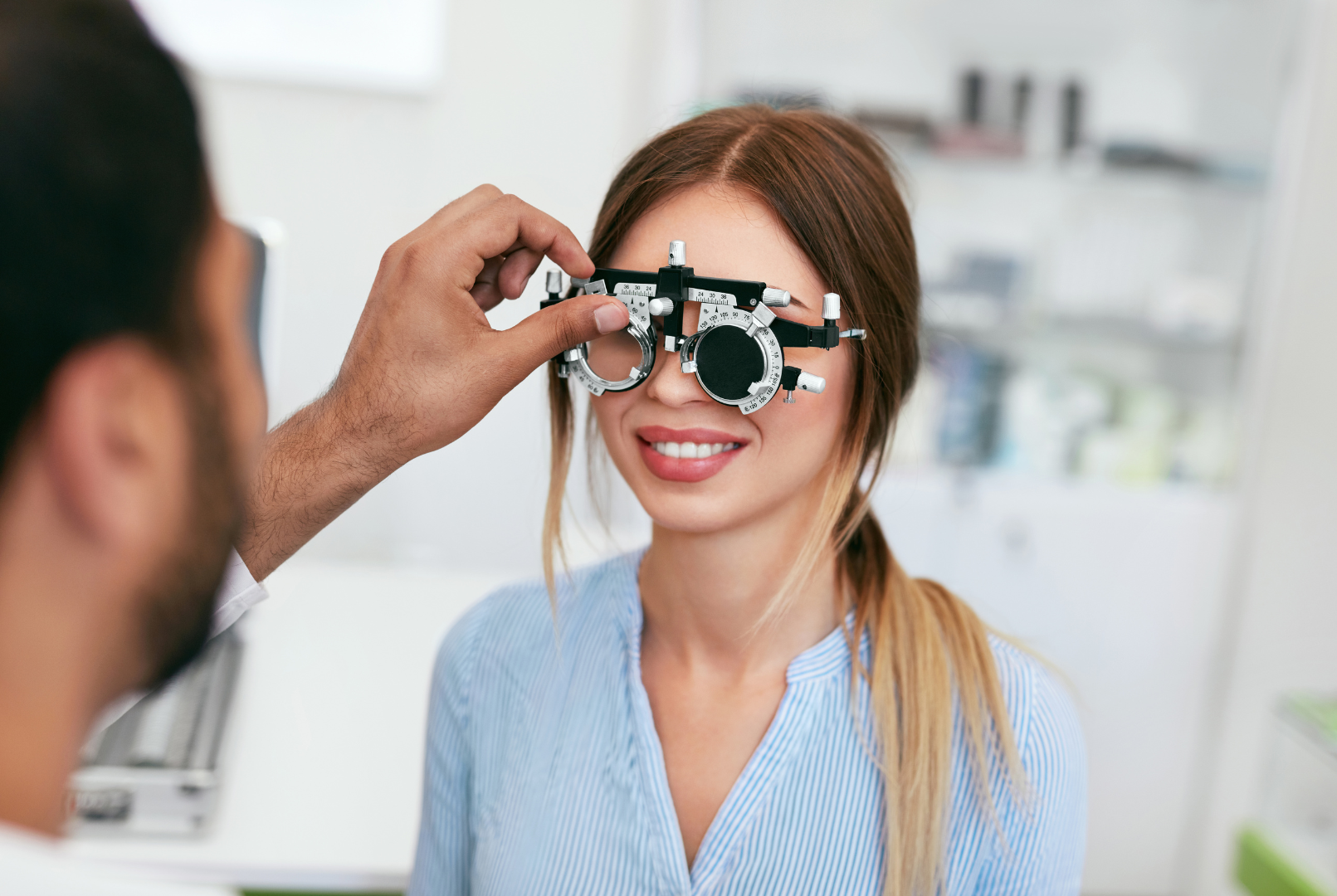 Optometrist using a phoropter on a patient for an eye exam; indoors.