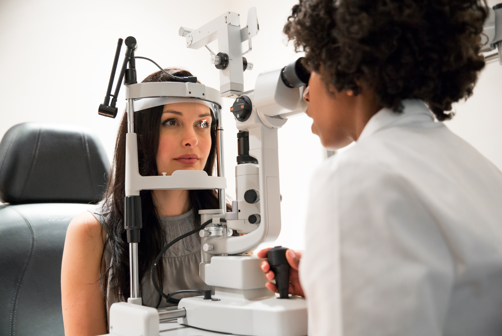 Woman having an eye exam by a doctor using a slit lamp in an examination room.