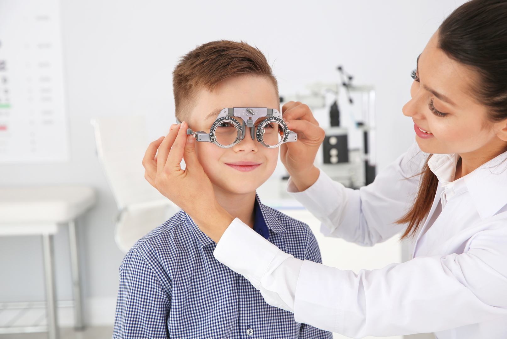 Optometrist adjusts a trial frame on a young patient in an eye exam room.