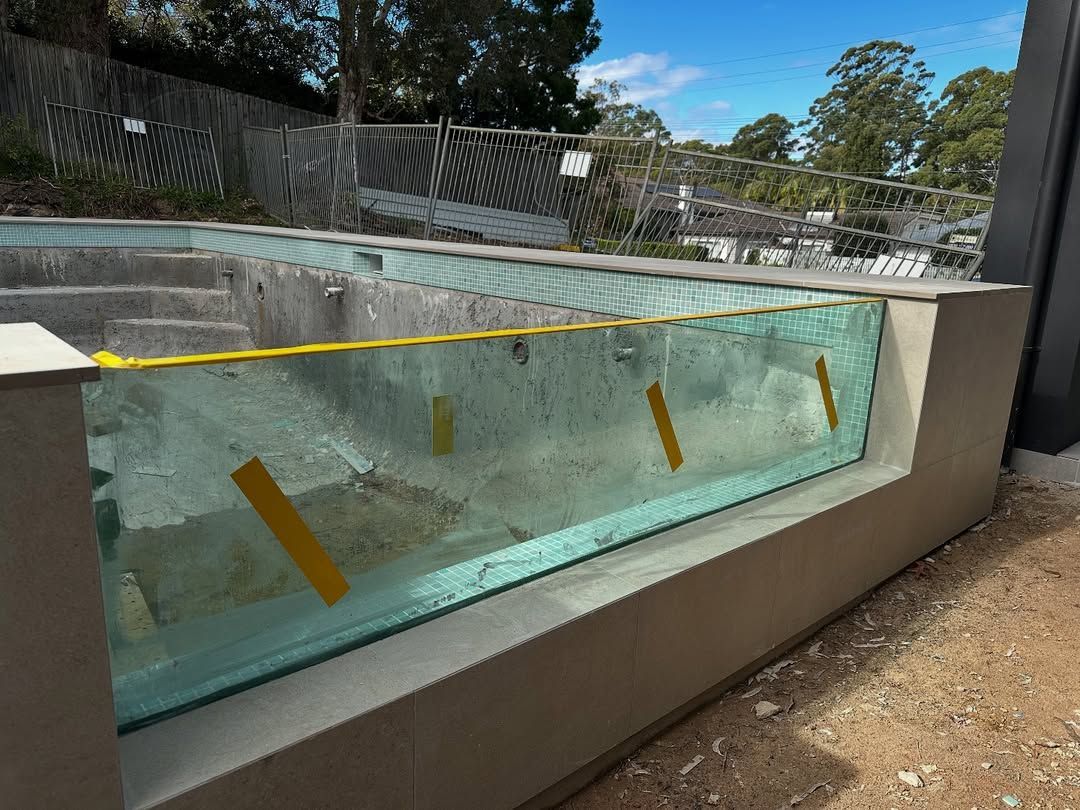 Partially Built Swimming Pool With a Glass Side Panel and Yellow Tape — All Glass Balustrading Systems in Central Coast, NSW
