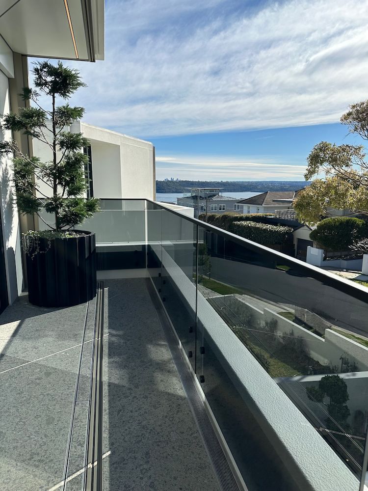 A Balcony With a Glass Railing and a Potted Plant on It — All Glass Balustrading Systems in Chatswood, NSW