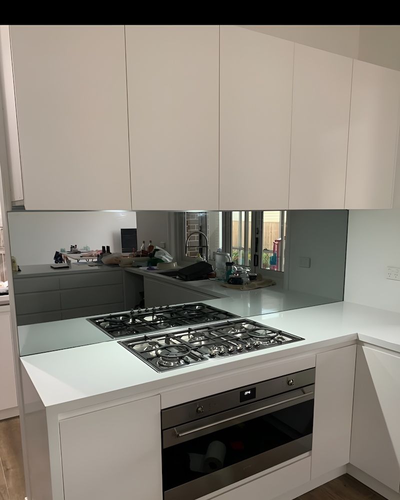 A Kitchen With White Cabinets, a Stove Top Oven, and a Large Mirror — All Glass Balustrading Systems in Wetherill Park, NSW