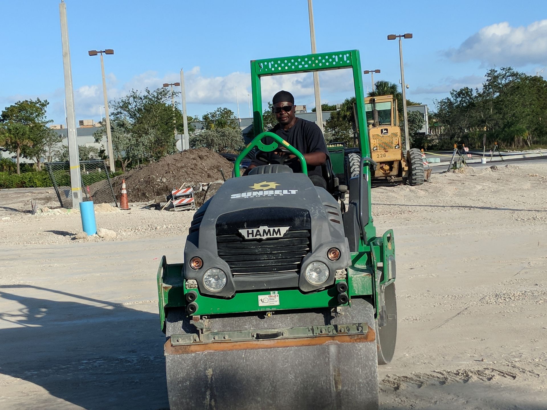 Construction workers smoothing wet concrete with a power trowel at a job site with machinery in the background.