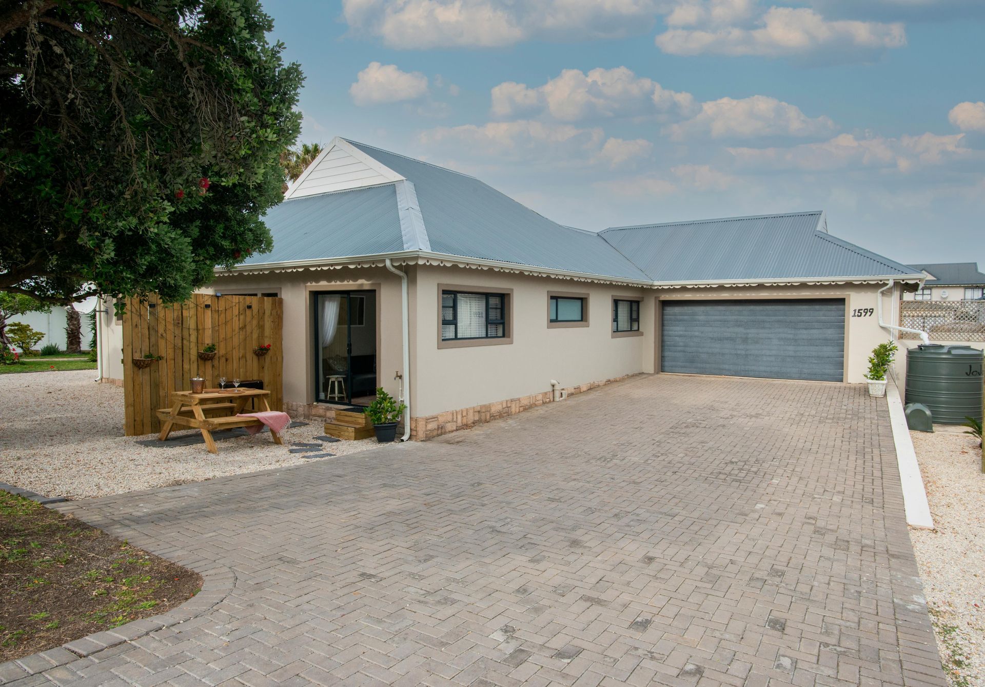 A cream-colored house with a blue metal roof, a garage, a paved driveway, and a small wooden patio area.