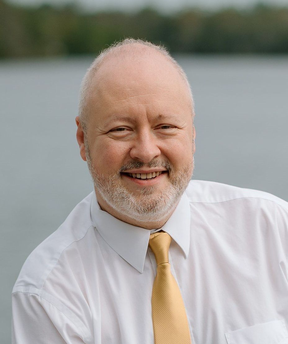 Matthew wearing a white shirt and a yellow tie.