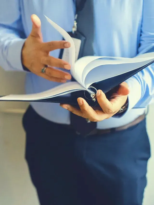 A man in a blue shirt and tie is holding a binder in his hands.