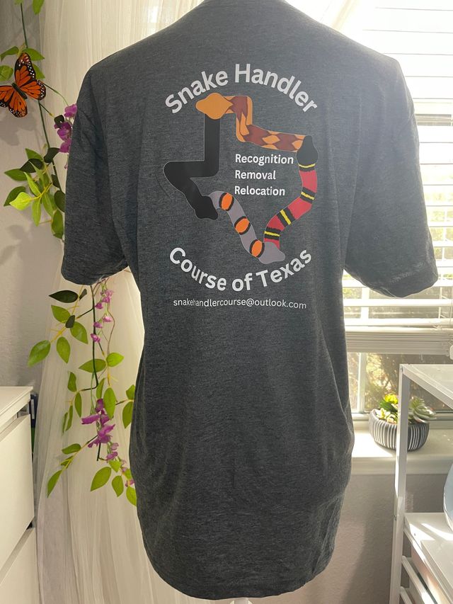 Black T-shirt on hanger with snake handler graphic and Course of Texas text, in front of a window